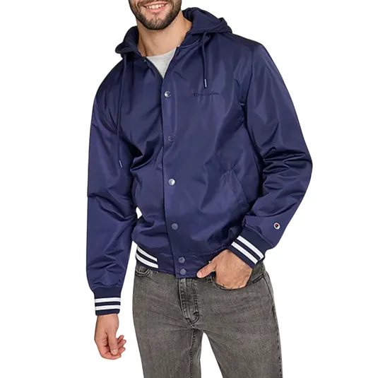 A man wears a navy blue hooded jacket with front snap buttons and striped cuffs and waistband, paired with gray jeans.