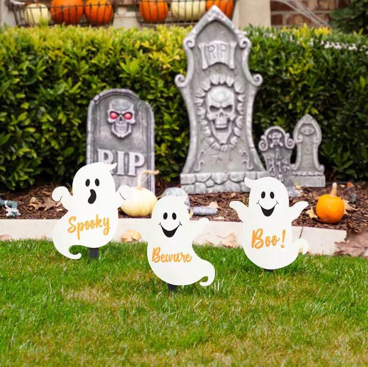 Three decorative ghost signs with the words \“Spooky,\“ \“Beware,\“ and \“Boo!\“ stand on a lawn with tombstone decorations in the background.