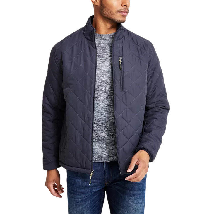 A man is wearing a dark quilted jacket with a front zipper and zippered chest pocket, paired with a gray sweater and blue jeans.