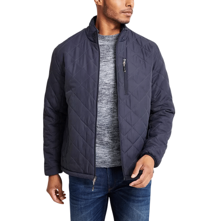 A man is wearing a dark quilted jacket with a front zipper and zippered chest pocket, paired with a gray sweater and blue jeans.