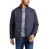 A man is wearing a dark quilted jacket with a front zipper and zippered chest pocket, paired with a gray sweater and blue jeans.