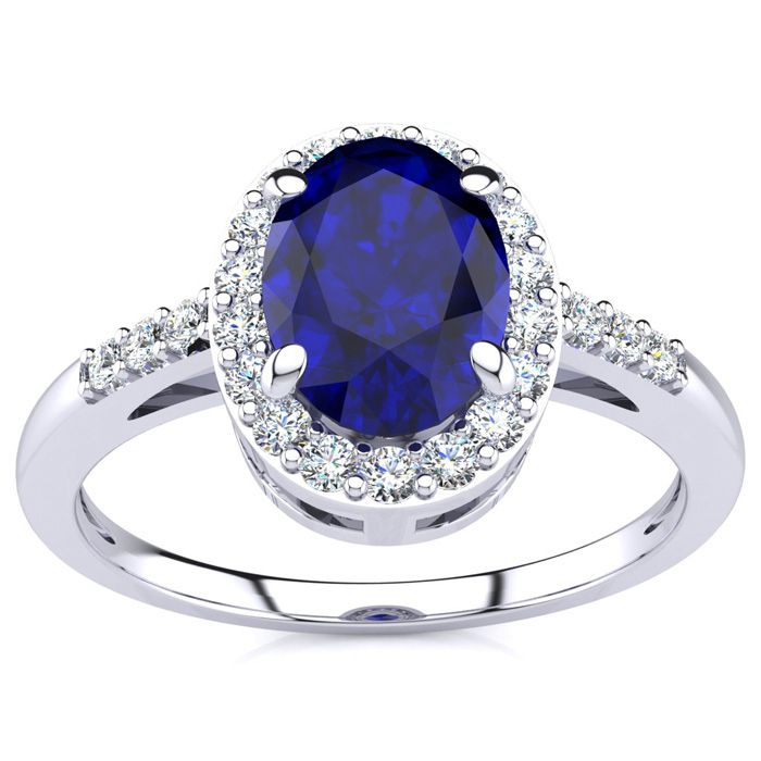 A white gold ring featuring a 1-carat oval blue sapphire center stone, surrounded by a halo of small round diamonds, with additional diamonds set along the band for added sparkle.