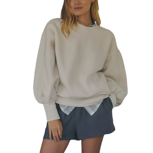 A cream-colored, slouchy crew-neck sweatshirt featuring long sleeves and a relaxed fit, layered over a plaid shirt with navy shorts.