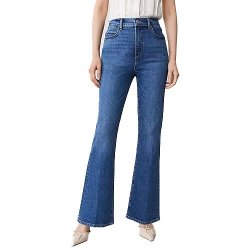 A person is wearing blue flared jeans paired with beige pointy-toed heels and a white blouse.