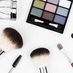 Makeup palette with various shades, eyelash curler, and an assortment of cosmetic brushes on a white background.