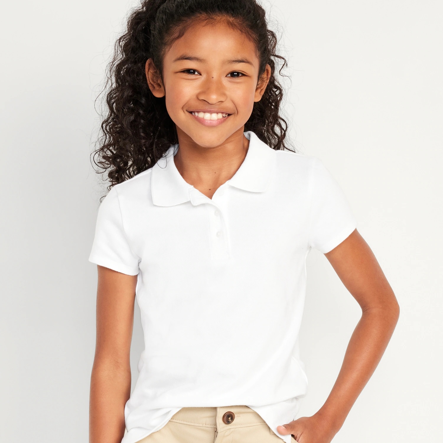 A young girl is smiling and wearing a white polo shirt and khaki pants.