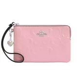 A pink Coach wristlet with embossed logo pattern, equipped with a zipper closure and a heart charm attached to the strap.
