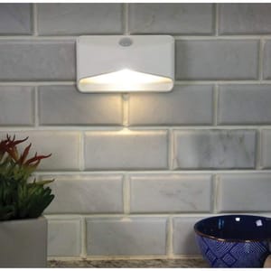 Wall-mounted LED night light with motion sensor, placed on a tiled surface, next to a small plant pot and a blue bowl.