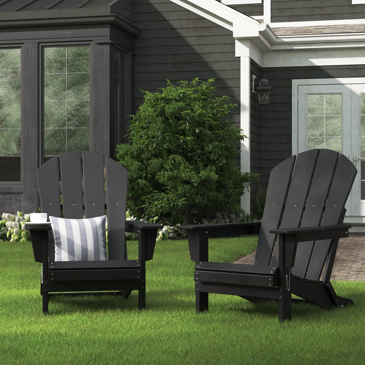 Two black Adirondack chairs are on a lawn, one with a striped cushion. A small white cup rests on the arm of one chair.