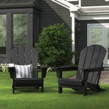 Two black Adirondack chairs are on a lawn, one with a striped cushion. A small white cup rests on the arm of one chair.