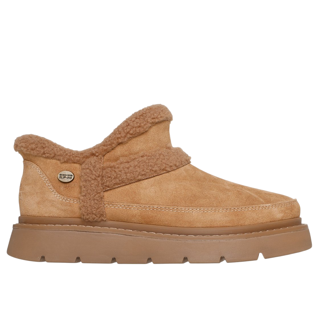 Tan suede slip-on shoe with a thick, textured sole and shearling trim. Embellished with a small metallic \“Skechers SLIP-INS\“ tag on the side.
