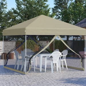A beige canopy tent with open mesh sides covers a white table and several white plastic chairs, set on a stone patio surrounded by trees and a wooden fence.