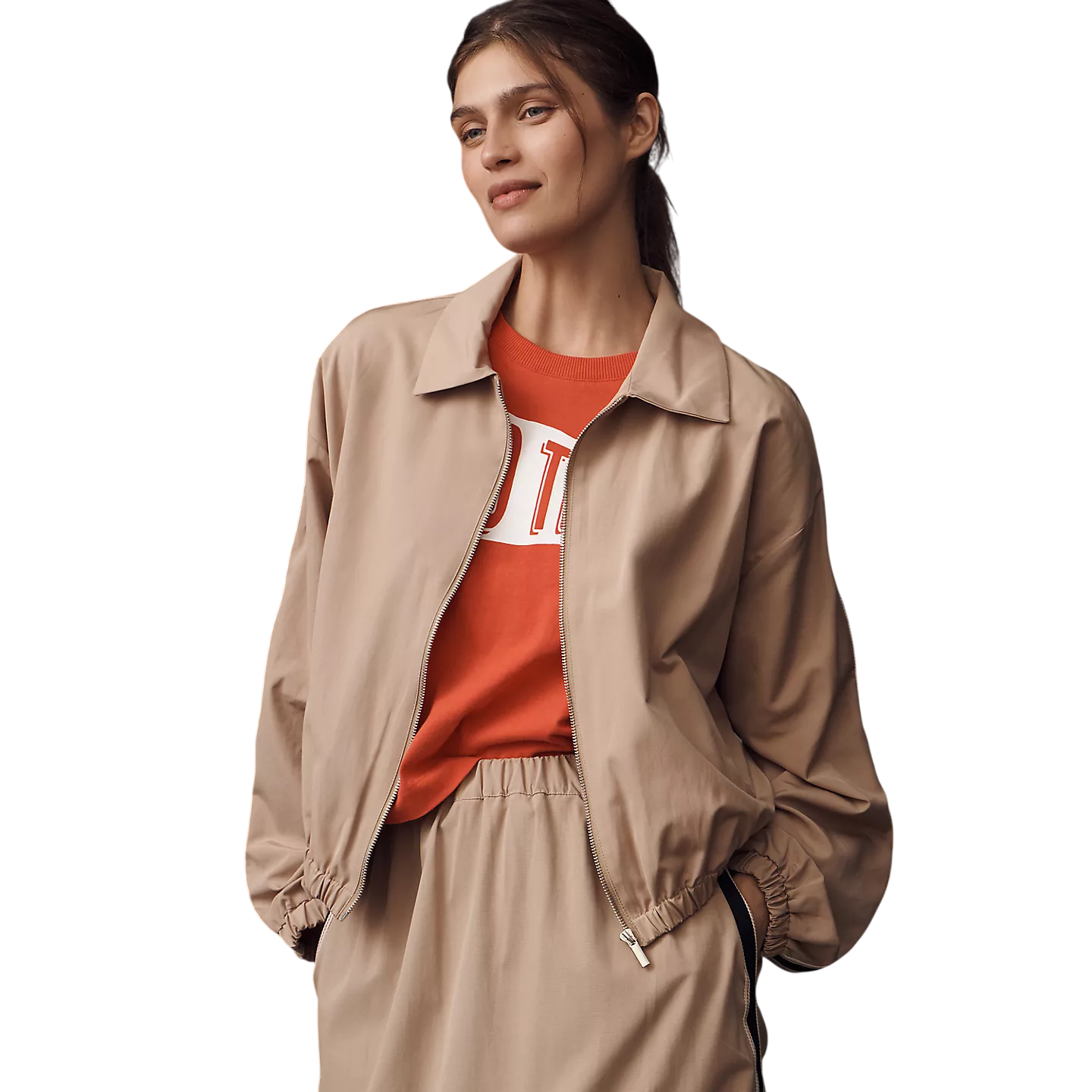 A woman is wearing a beige zip-up jacket and matching pants, paired with an orange top underneath.