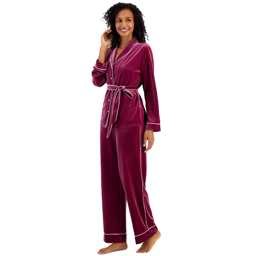 A woman models a two-piece pajama set with a long-sleeve, V-neck top and matching pants in a deep burgundy velvet material, accented with a contrasting trim and waist tie.