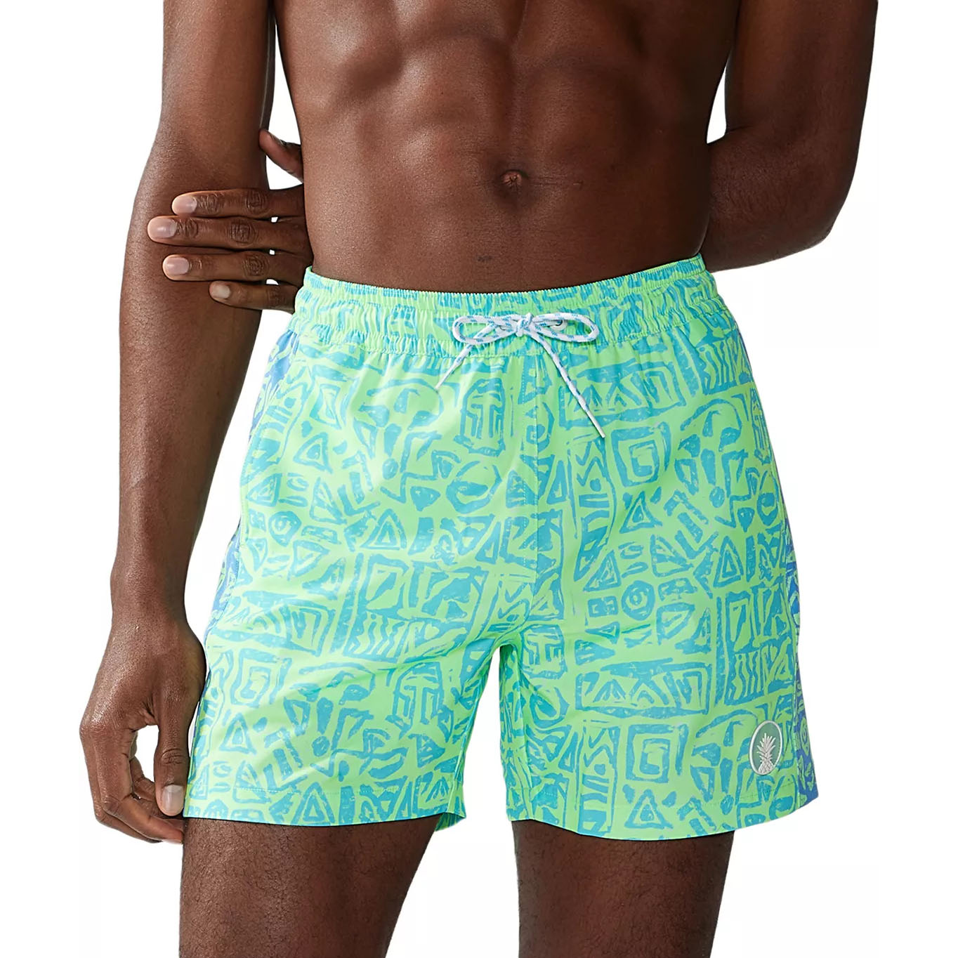 Chubbies Classic 5.5\“ Swim Trunks feature a bright green and blue geometric pattern, elastic waistband with a drawstring, and a small logo on the leg.