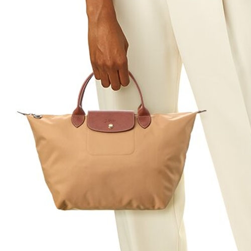 A beige tote bag with maroon handles and trim, held by a person wearing a white outfit.