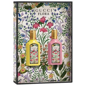 Gucci Flora Gift Set features two perfume bottles in yellow and pink, each adorned with a floral pattern. The background also showcases a vibrant array of flowers and leaves, reflecting the brand's signature floral design.