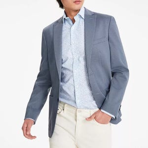 A slim-fit sport coat in a textured knit with a notched lapel and two-button front closure; presented in shades of blue and paired with a patterned shirt and light-colored trousers.
