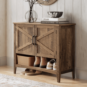 A rustic wooden shoe cabinet with black handles features a shelf holding boots, sneakers, and a wicker basket, topped with decor items like books, a bowl, and a glass vase with branches, set on a light wooden floor next to a textured rug.