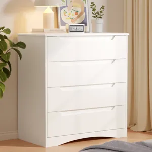 A white four-drawer dresser is topped with a lamp, digital clock, and framed artwork. A potted plant is nearby, and the setup is against a light-colored curtain.