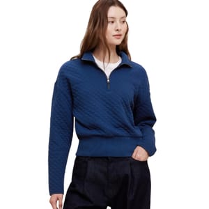 A woman is wearing a blue quilted pullover with a half-zip closure and ribbed cuffs and hem, paired with dark pants.