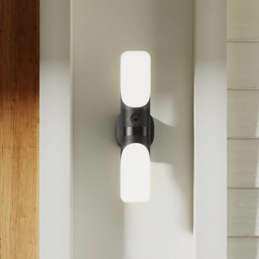 A wall-mounted security light with built-in camera between two illuminating panels.