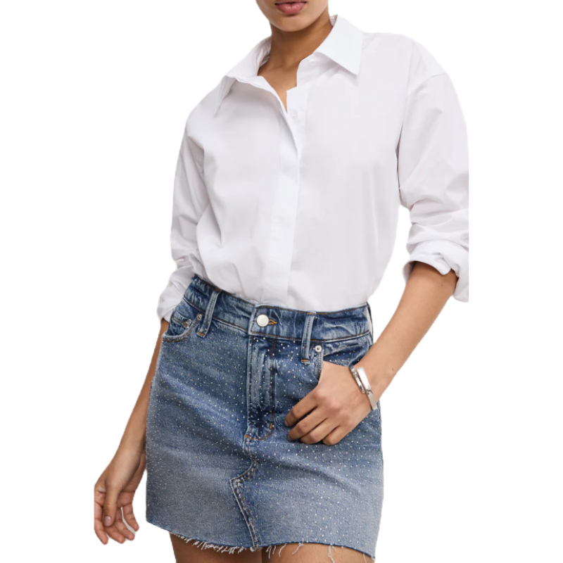 A denim mini skirt with a frayed hem featuring a subtle sparkle from embedded small rhinestones, paired with a classic white button-up shirt.