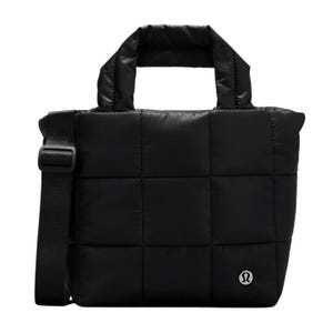 A black, quilted tote bag featuring a shoulder strap and top handles, with a small, circular logo on the front.