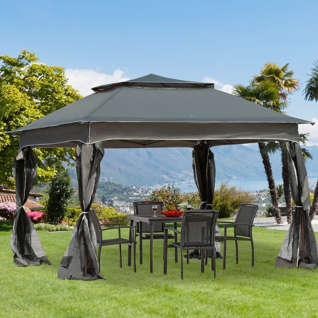 A gazebo with a gray canopy and mesh curtains is set up over a patio table and chairs on a grassy lawn, overlooking a scenic view of mountains and a lake.