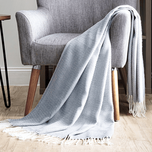 A gray armchair with wooden legs is accompanied by a light blue textured throw blanket hanging over its side, set on a wooden floor.