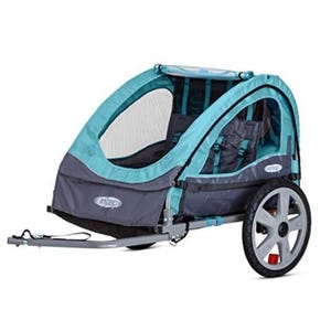 A teal and gray bike trailer for kids featuring a mesh cover, two seats with harnesses, and two large rear wheels with reflectors. It includes a tow bar for attachment to a bicycle.
