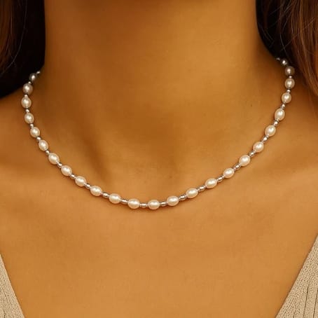 A delicate pearl necklace composed of evenly spaced small, round pearls resting against the neck. The close-up highlights the elegant simplicity and classic design.