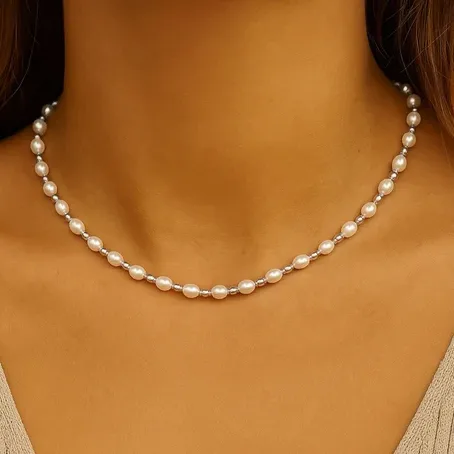 A delicate pearl necklace composed of evenly spaced small, round pearls resting against the neck. The close-up highlights the elegant simplicity and classic design.