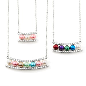 Three necklaces featuring colorful pearl-like beads, each set between two curved bars adorned with small clear gemstones.