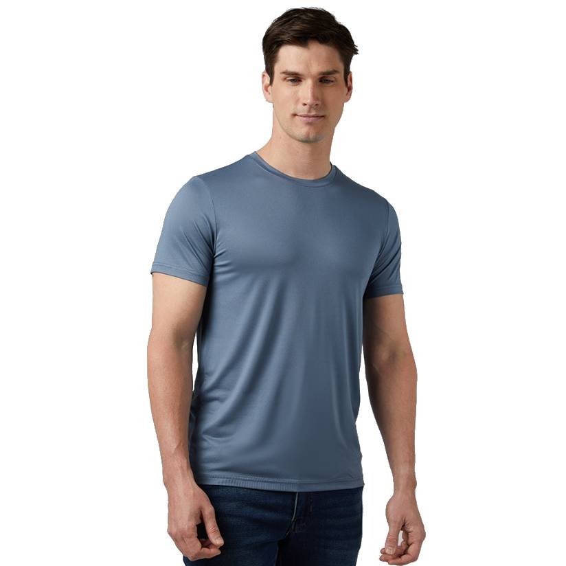 A man wears a light blue, short-sleeve athletic T-shirt paired with dark jeans, standing against a plain white background.