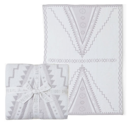 A soft Barefoot Dreams throw blanket with a geometric pattern in light gray and white, wrapped with a branded ribbon. The design features large V-shaped motifs with a southwestern style.