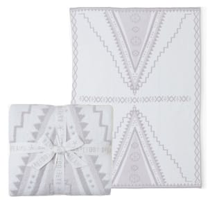 A soft Barefoot Dreams throw blanket with a geometric pattern in light gray and white, wrapped with a branded ribbon. The design features large V-shaped motifs with a southwestern style.