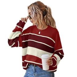 A woman wearing a red and cream striped sweater paired with blue jeans holds a coffee cup and adjusts her sunglasses. Her hair is styled in a ponytail.