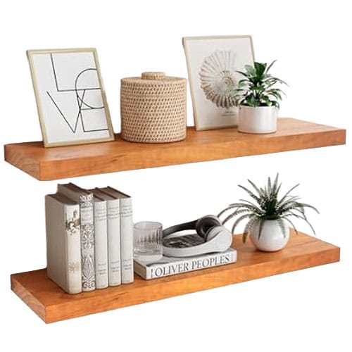 Two wooden floating shelves display framed art, a woven basket, potted plants, a stack of books, and decorative items including a coiled rope and a glass cup.