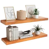 Two wooden floating shelves display framed art, a woven basket, potted plants, a stack of books, and decorative items including a coiled rope and a glass cup.