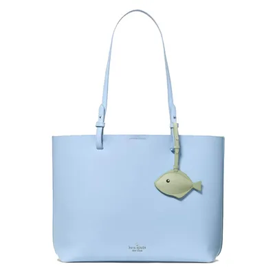 A light blue tote bag with a long strap and a small green fish-shaped charm.
