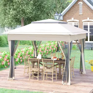 A beige outdoor gazebo with a mesh curtain encloses a wooden dining table and chairs, set on a wooden deck. A traditional brick house and a garden with flowers and greenery are visible in the background.