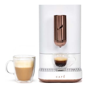 The Cafe Affetto Smart Espresso Machine is a sleek, white espresso maker with copper accents, featuring a modern design and the ability to brew espresso into a glass cup. It includes an additional glass with frothy coffee beside it.