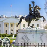 A statue of a rider on horseback is in front of the White House, with a cannon nearby and a U.S. flag flying above the building.