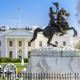 A statue of a rider on horseback is in front of the White House, with a cannon nearby and a U.S. flag flying above the building.