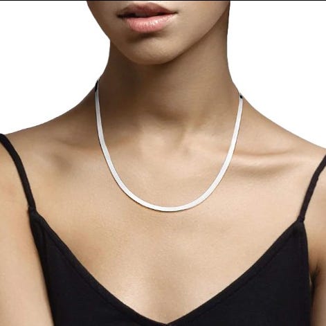 A woman wearing a simple, sleek silver necklace with a smooth, thin chain.