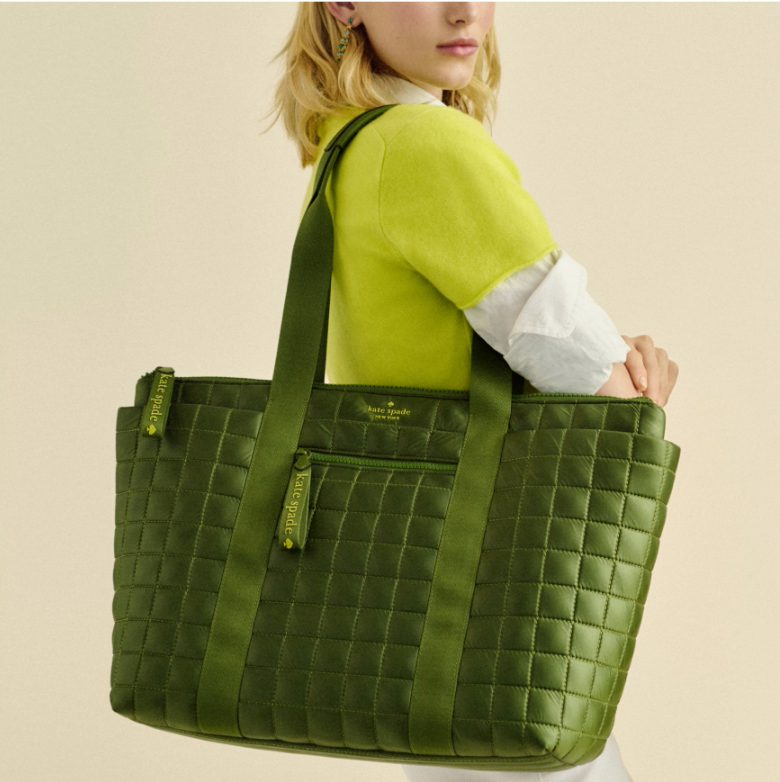 A woman is carrying a large green quilted tote bag over her shoulder.