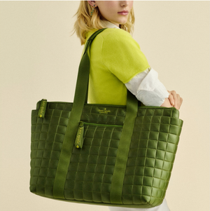 A woman is carrying a large green quilted tote bag over her shoulder.