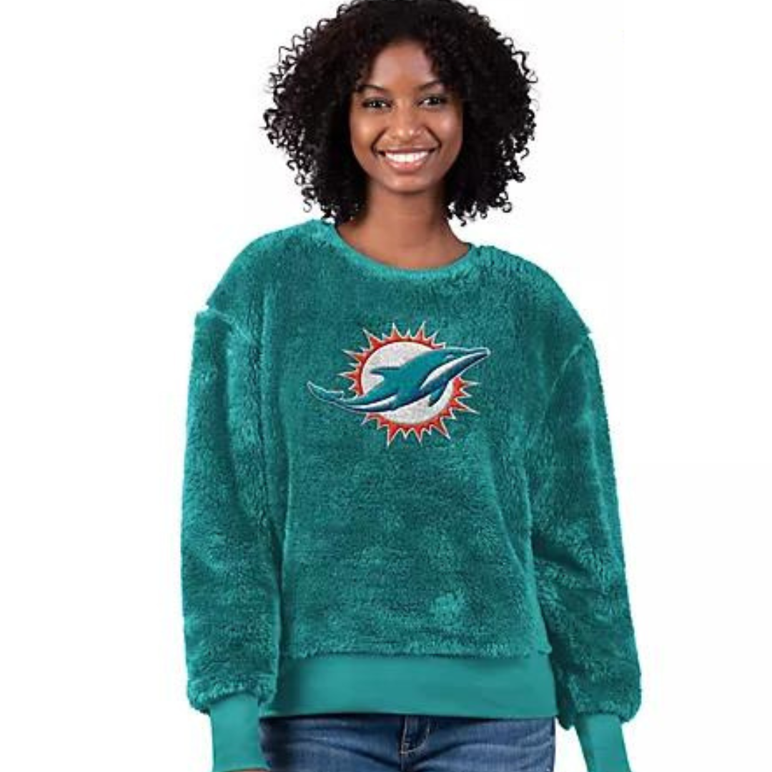 A woman is wearing a teal long-sleeve crewneck sweater with a Miami Dolphins logo on the front.