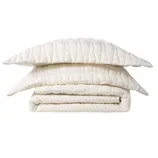 A folded, quilted, cream-colored bedding set comprising a comforter and two matching pillowcases with a grid pattern.